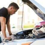 Man looking under hood of broken-down car