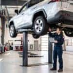 Certified Toyota technician inspecting a silver RAV4 on a vehicle lift during a routine maintenance schedule service.