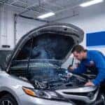 Toyota technician inspecting an open car hood with smoke to diagnose a car smell burnt rubber issue at the service center.