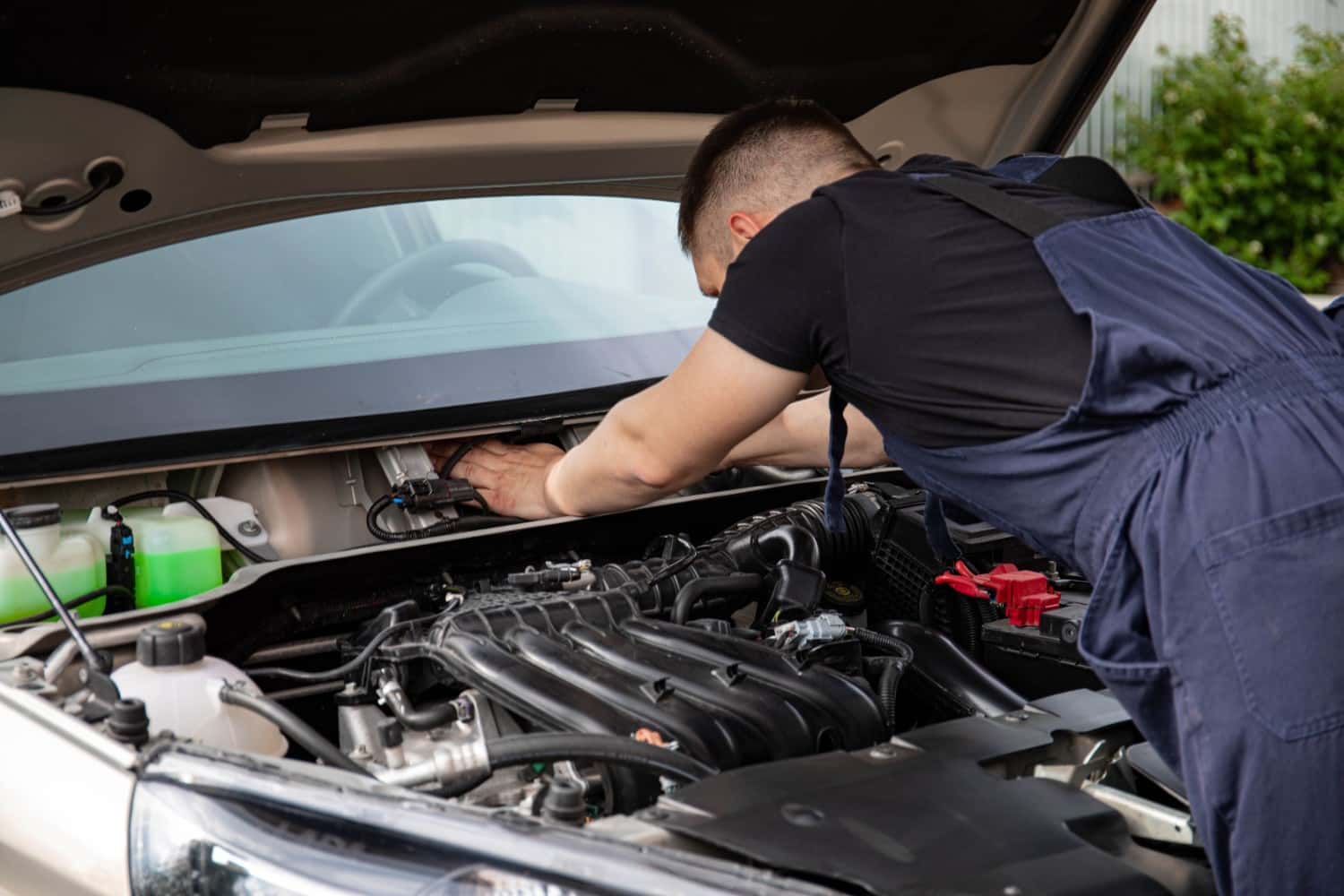 Automotive technician inspecting and cleaning a car engine bay during routine maintenance
