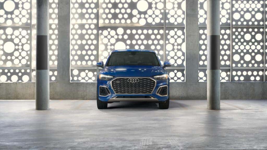2024 Audi Q5 in the color blue, parked in a parking garage with a perforated wall letting in light behind it.