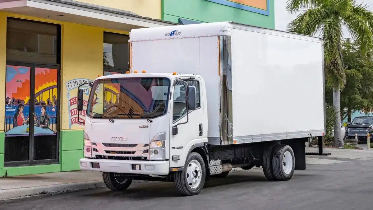 A white Isuzu NPR truck parked by a small restaurant