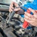 A man's hands attaching battery jumper cables to a dead car battery