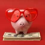 Piggy bank with heart sunglasses standing on stack of money