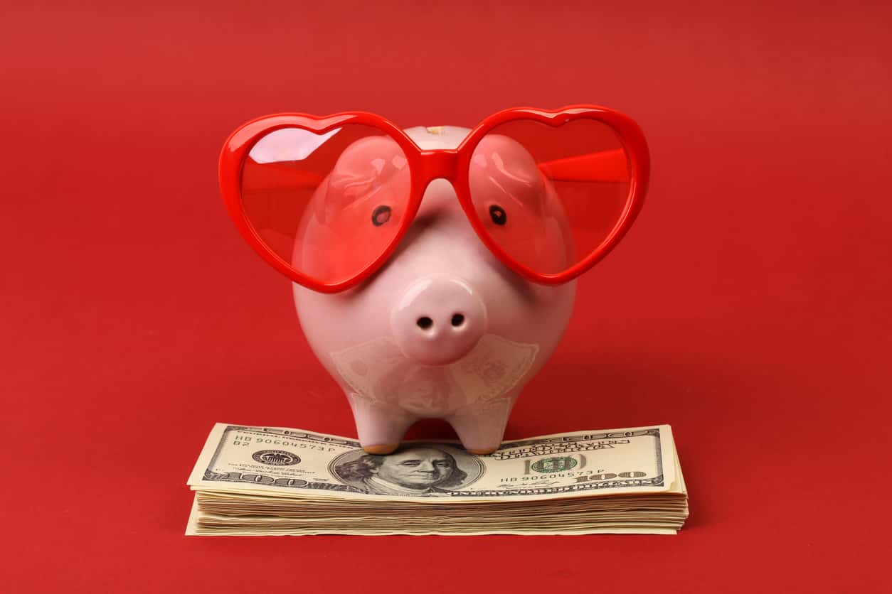 Piggy bank with heart sunglasses standing on stack of money