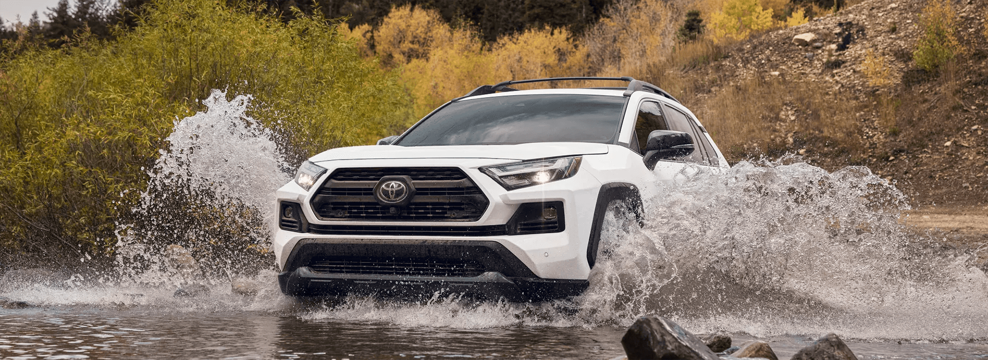 The new 2022 Toyota RAV4 in white driving over a stream.