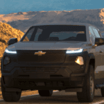 Front view of a Chevrolet Silverado Trail Boss pickup on a winding coastal mountain road at sunset, with LED light strip and rugged black grille.