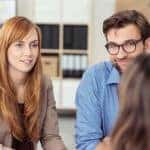 Investment broker meeting with a young couple in her office to discuss their financial needs, view from behind the agent of the couple