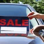 woman placing sale sign on car windshield