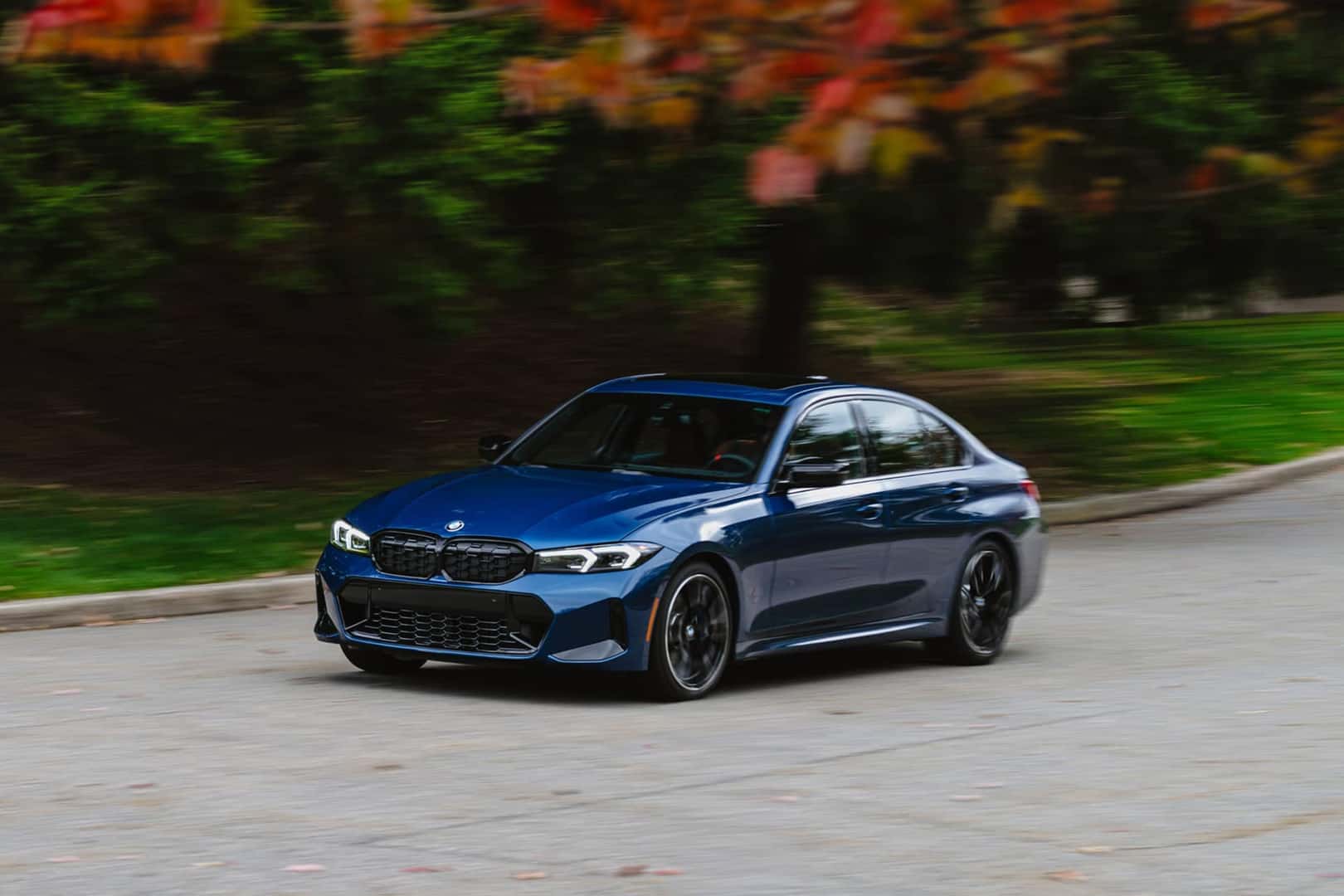 2026 blue bmw 3series driving on road in front of fall tree