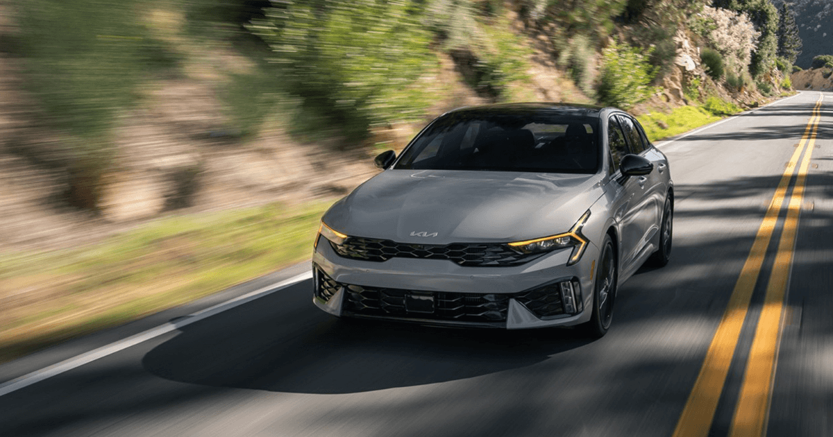 A gray 2025 Kia K5 driving down the road
