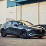 A Mazda 3 hatchback parked outside a warehouse, showcasing its stylish design and versatility.