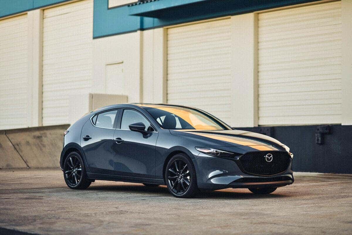 A Mazda 3 hatchback parked outside a warehouse, showcasing its stylish design and versatility.