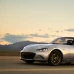 A 2024 Mazda MX-5 Roadster is cruising along a scenic road, showcasing its sleek design and sporty performance.