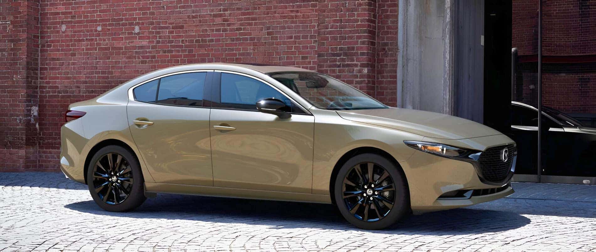 2025 Mazda3 Compact sedan parked in front of a rustic brick bruilding