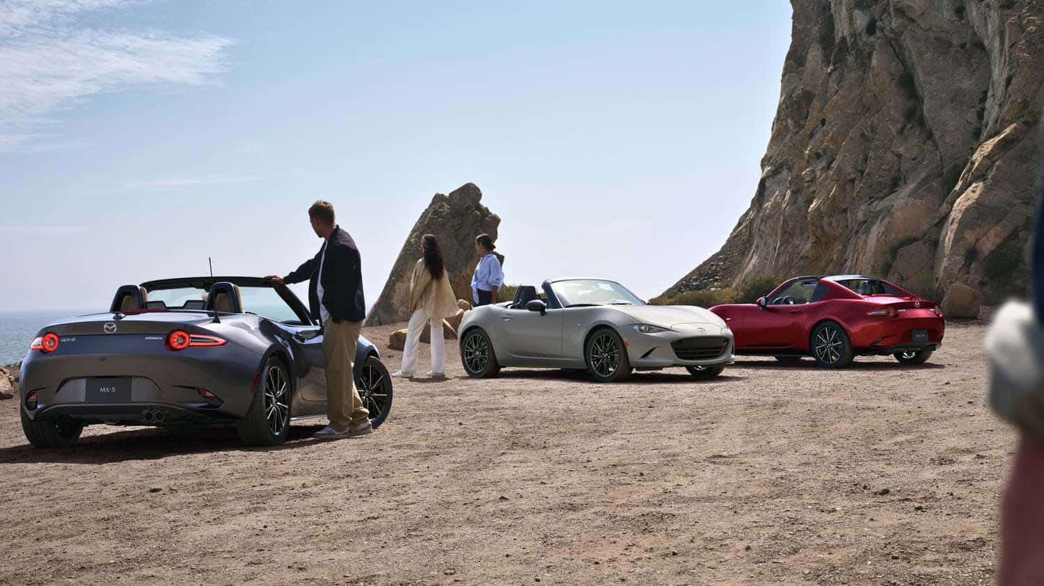 Three individuals pose beside their sleek Mazda Miata sports cars, showcasing their sleek and beautiful design.