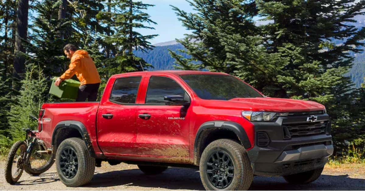 A Man Going Mountain Biking With His Red 2023 Chevrolet Colorado with Pine Trees and Mountains In The Background