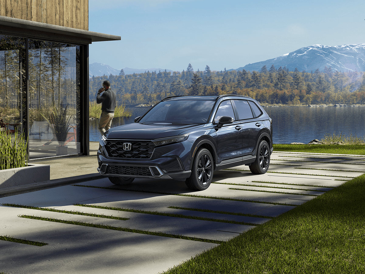 The new Honda CR-V sits parked near a house by a lake.