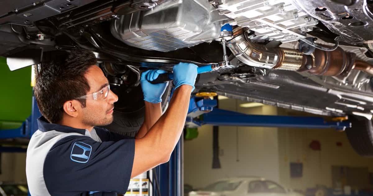 A Honda Service Technician performing maintenance on a vehicle on a lifted bed in the service center.