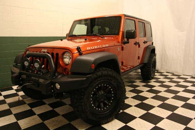 Front view of a customized Mango Tango [Orange] Jeep Wrangler Rubicon in a black-and-white checkered showroom