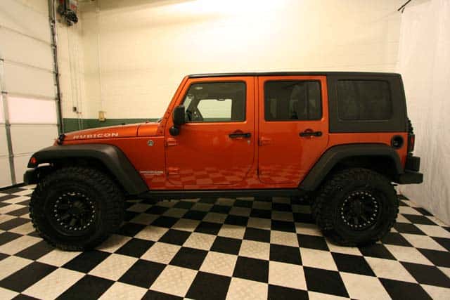 Side view of a customized Mango Tango [Orange] Jeep Wrangler Rubicon in a black-and-white checkered showroom