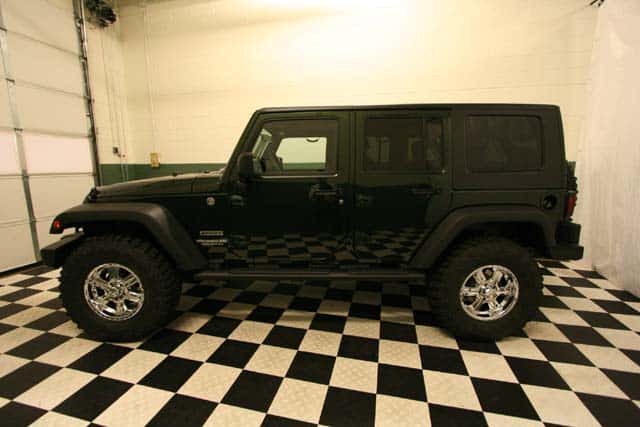 Side view of a customized Natural Green 4-door Jeep Wrangler in a black-and-white checkered showroom