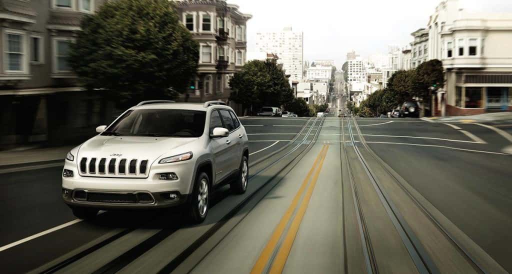 A white 2016 Jeep Cherokee driving on an empty city street.