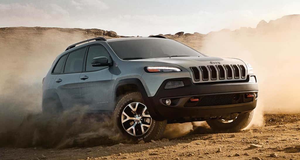 A gray 2016 Jeep Cherokee Trailhawk kicking up dirt in a field.