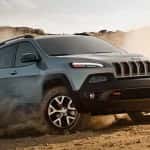 A silver 2016 Jeep Cherokee is kicking up sand on a desert track.