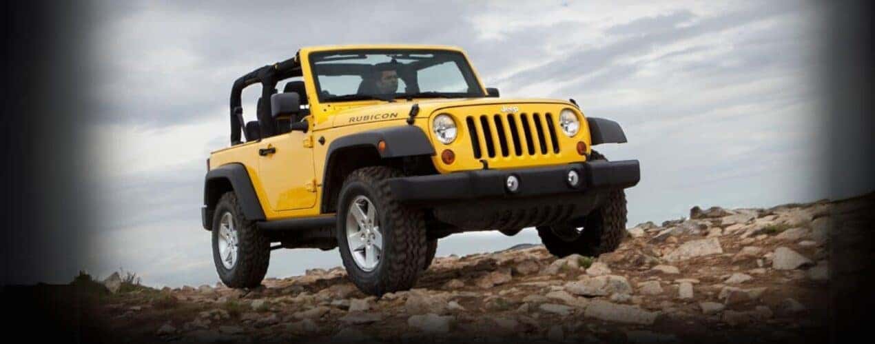 A yellow 2011 Jeep Wrangler Rubicon is shown parked off-road.