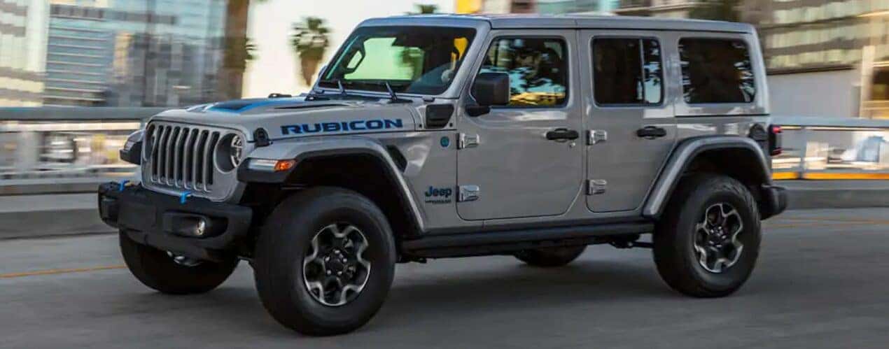 A silver 2021 Jeep Wrangler 4xe Rubicon is shown driving on a city street.