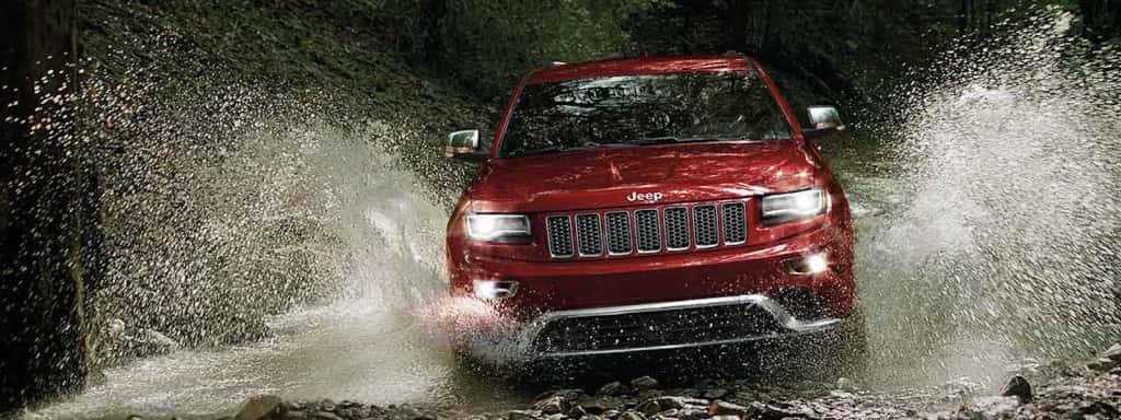 A red 2016 Jeep Grand Cherokee splashes through a puddle at nighttime