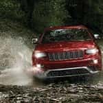 Front-view of a red Jeep Cherokee splashing through water on a wooded trail