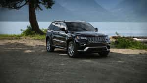 A black 2016 Jeep Grand Cherokee Summit is parked in front of a lake and mountains.