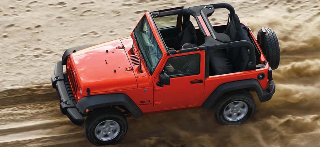 A red 2016 Jeep Wrangler without a top is driving on a sandy trail and is shown from above.