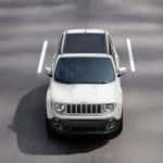 A white 2015 Jeep Renegade is driving on an empty road and is shown from above.