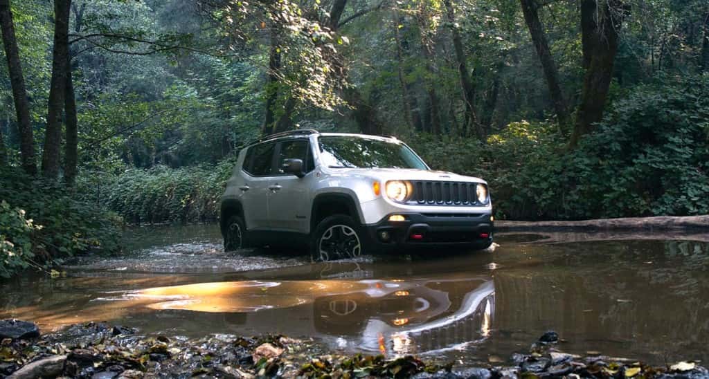 A silver 2015 Jeep Renegade is crossing a puddle on a woodland trail.