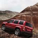 A red 2014 Jeep Patriot from a Jeep dealer in Colorado is climbing rocks in a desert.