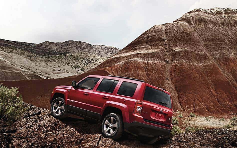 A red 2014 Jeep Patriot from a Jeep dealer in Colorado is climbing rocks in a desert.