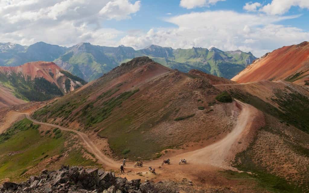Motorcycles parked at the bottom of a dirt road going over red mountains