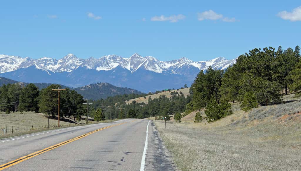 A small highway leading to large snow-capped mountains in the distance