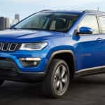 A blue 2017 Jeep Compass Longitude is driving with a city in the distance. Check one out at a Jeep dealer in Colorado.