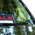 Red, black, and white "SALE" sign on the windshield of a black vehicle