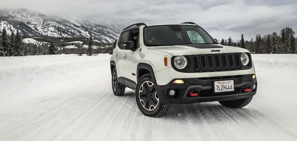 A white 2017 Jeep Renegade is driving on a snowy road.