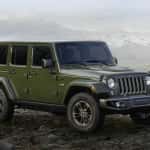 A green Jeep Wrangler Unlimited from Jeep dealers in Colorado is parked in front of misty mountains.