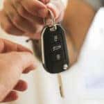 Hand holding out a car key while another hand reaches to grab it