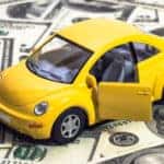 Yellow toy car with the door open sitting on a pile of one-hundred-dollar bills