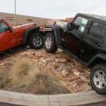 Two Jeep Wranglers, one red and one black, climbing a hill in front of Faricy Chrysler Jeep Jeep Dealership in Colorado Springs.