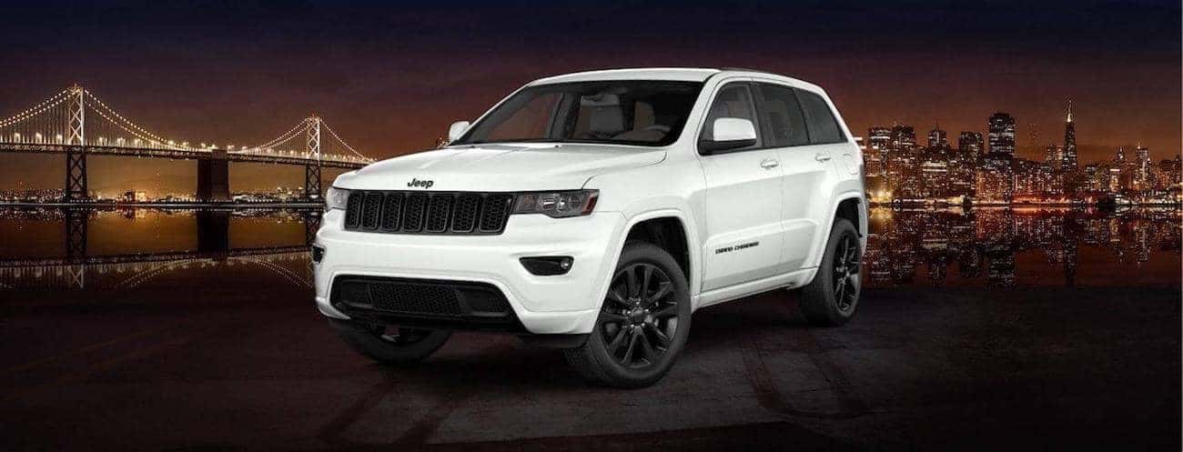 A white 2017 Jeep Grand Cherokee Altitude in front of a city at night