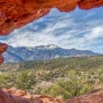 Red rock wall with a hole in the middle revealing tall Colorado mountains and trees